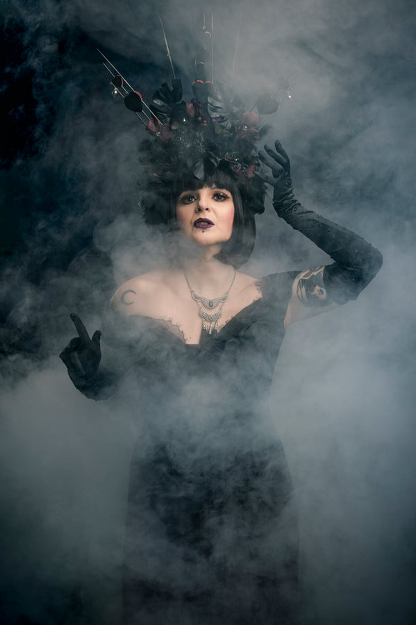 Anaïs Lune in black feather headdress and corset amidst fog