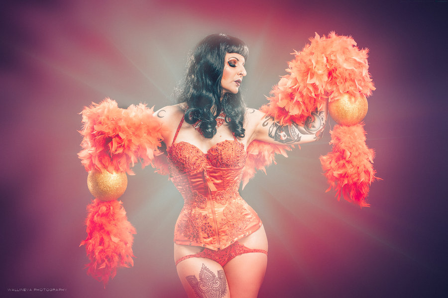 Anaïs Lune in orange feather boas against a magenta background