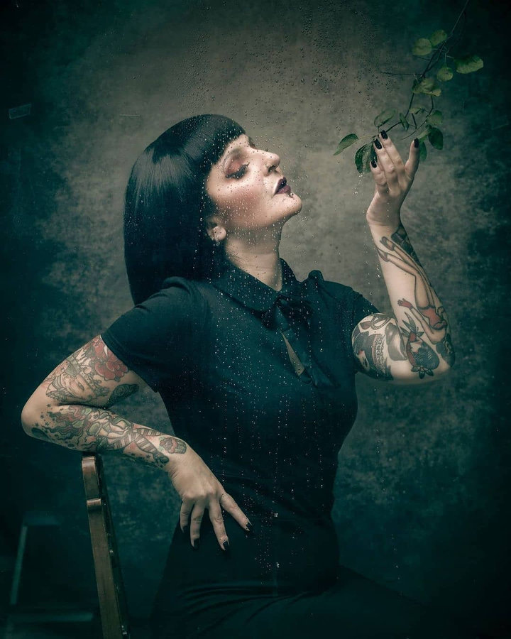 Anaïs Lune in high-neck black dress holding a botanical stem
