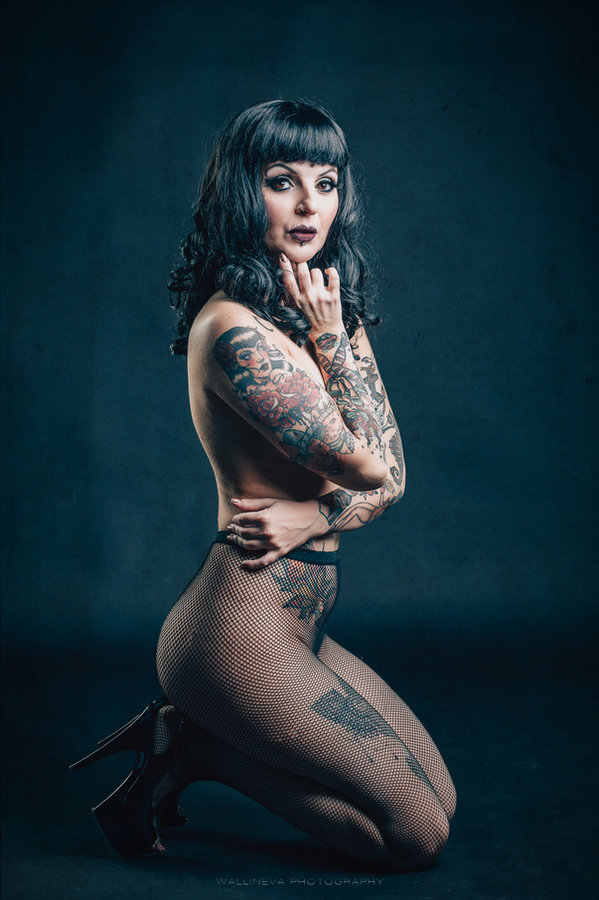 Anaïs Lune kneeling side view in dark lingerie, teal backdrop
