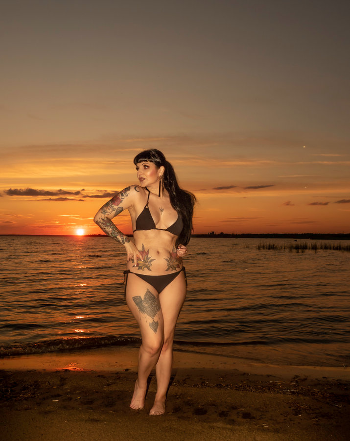 Anaïs Lune in a black bikini on a beach at sunset