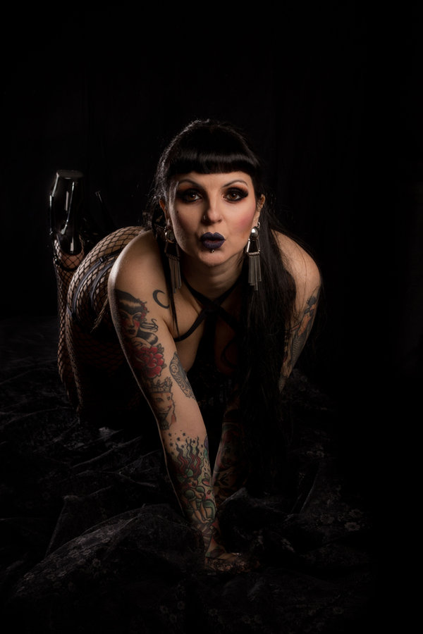 Anaïs Lune kneeling, leaning toward the camera, low-key light