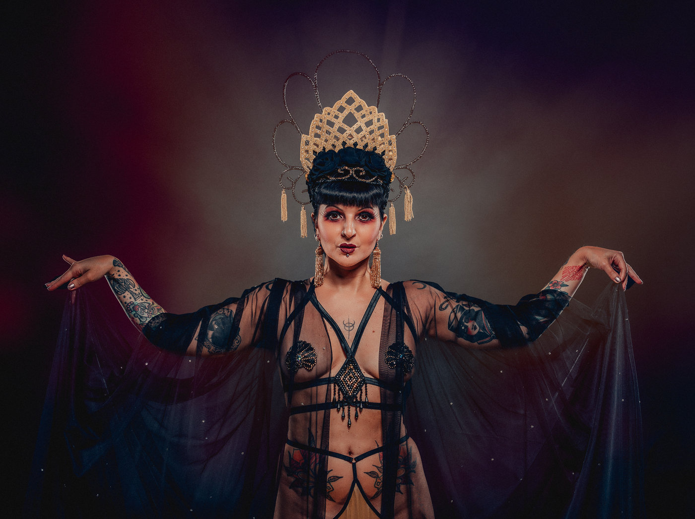 Anaïs Lune on stage, arms outstretched in a golden spotlight, wearing a beaded headpiece and feathered cape