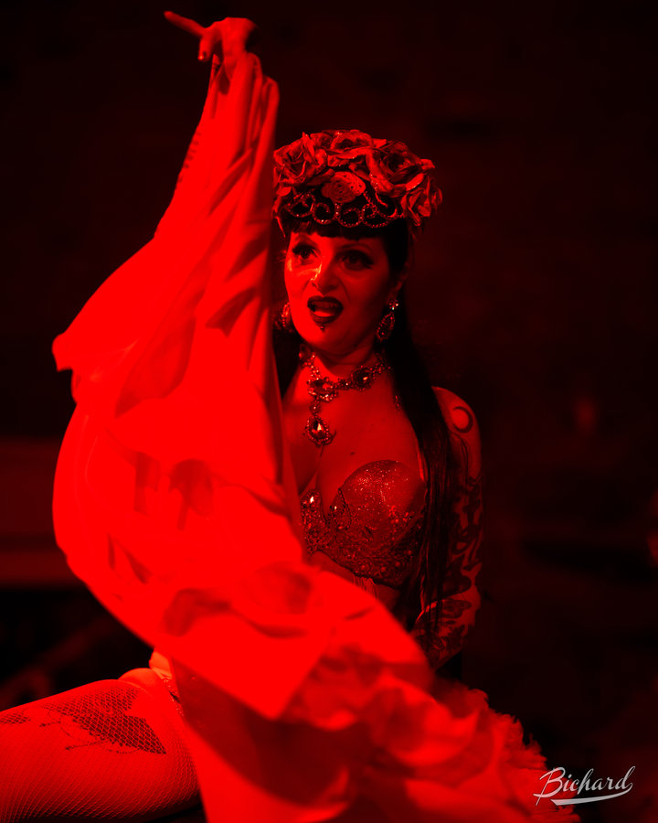 Anaïs Lune waving a red flowing fabric wrap under warm stage lights