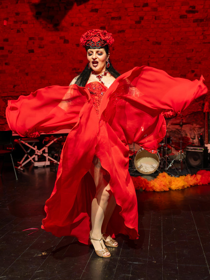 Anaïs Lune with outstretched red winged sleeves and a rose headpiece on a dark stage