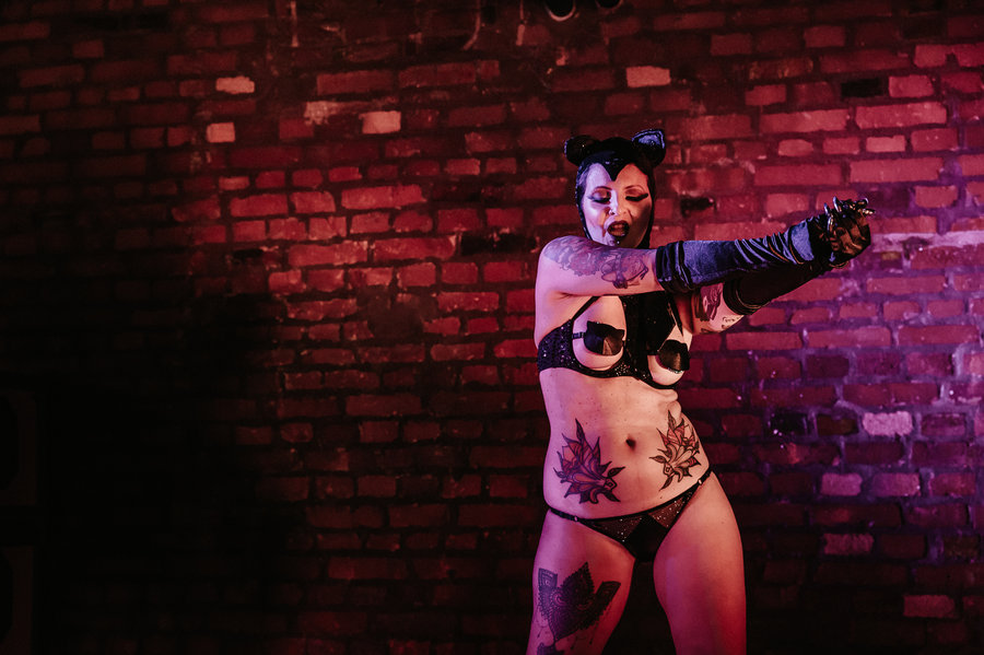 Anaïs Lune posing against a brick wall in dark lingerie and long gloves