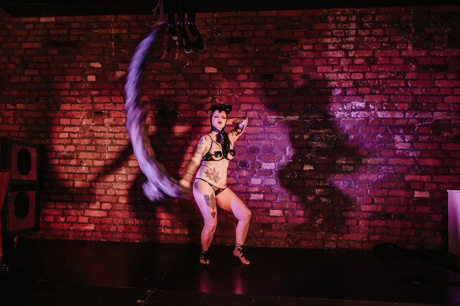 Anaïs Lune posing in a suspended aerial hoop against a brick wall