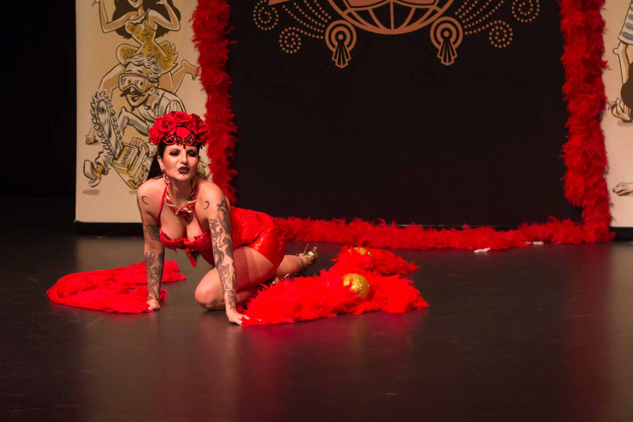 Anaïs Lune in red crawling across a dark stage flanked by a red feather boa
