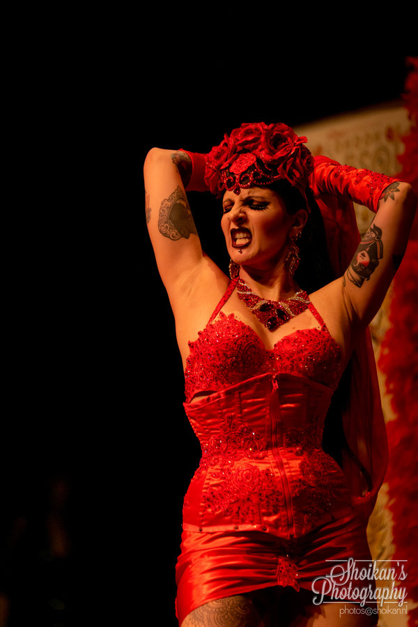 Anaïs Lune in a red corset dress and floral headdress, hands near her face