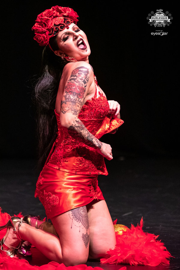Anaïs Lune kneeling in a shiny red dress with a rose crown and red feather boa