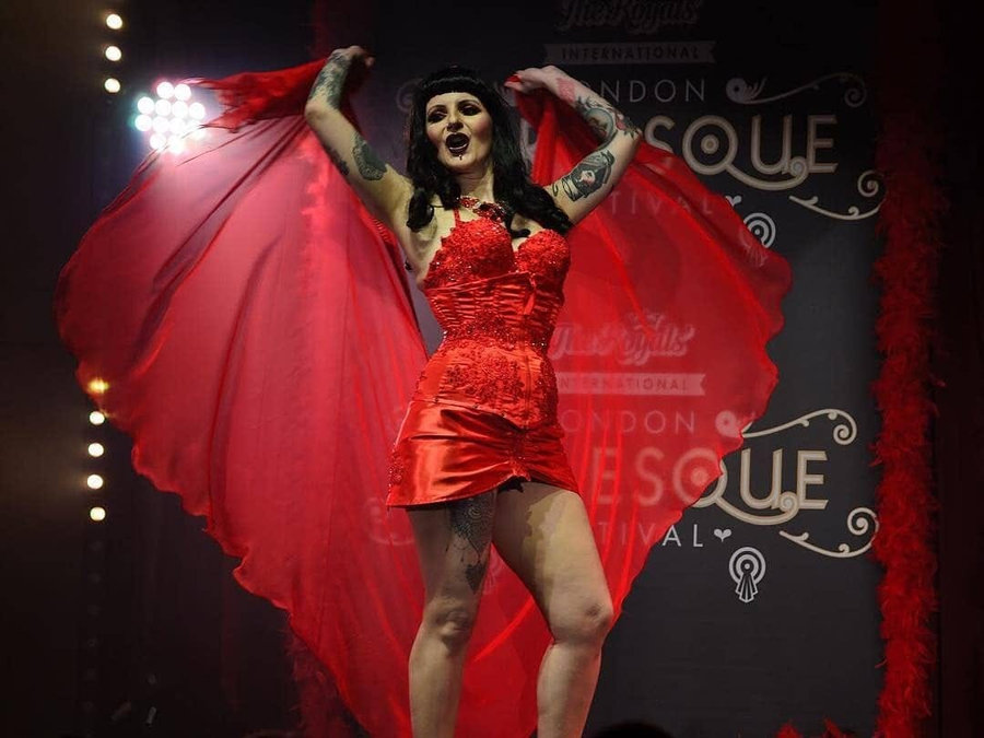 Anaïs Lune smiling with arms raised, spreading a large red cape