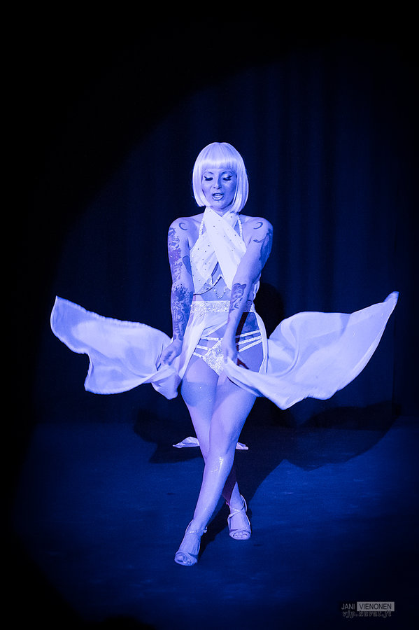 Anaïs Lune in a blonde bob and fluttering white dress under a blue spotlight