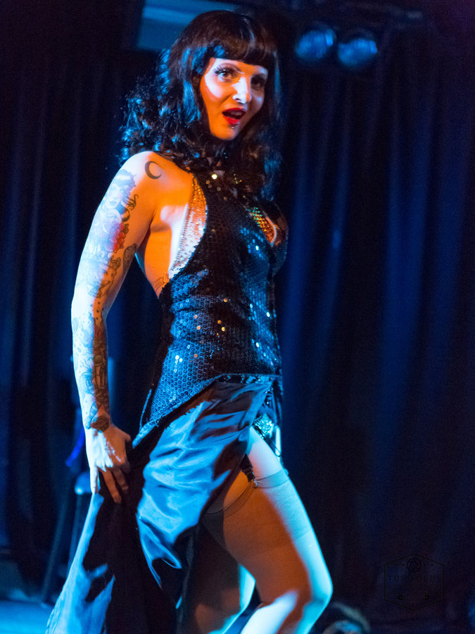 Anaïs Lune in a sparkling dress smiling under blue stage lights