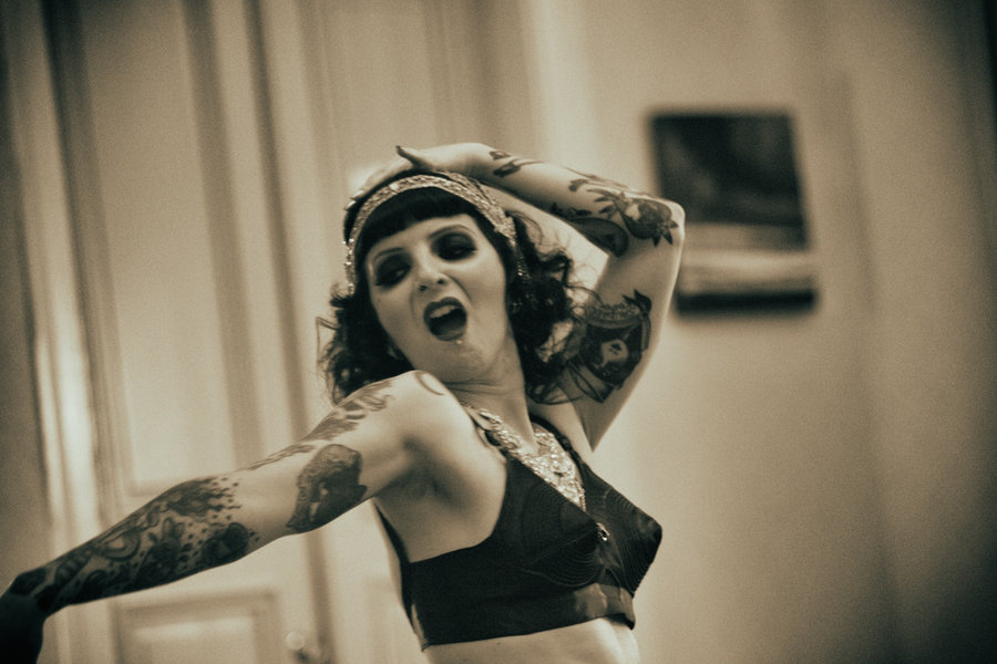Toned close-up of Anaïs Lune reaching toward the camera in a dark bra top and headpiece