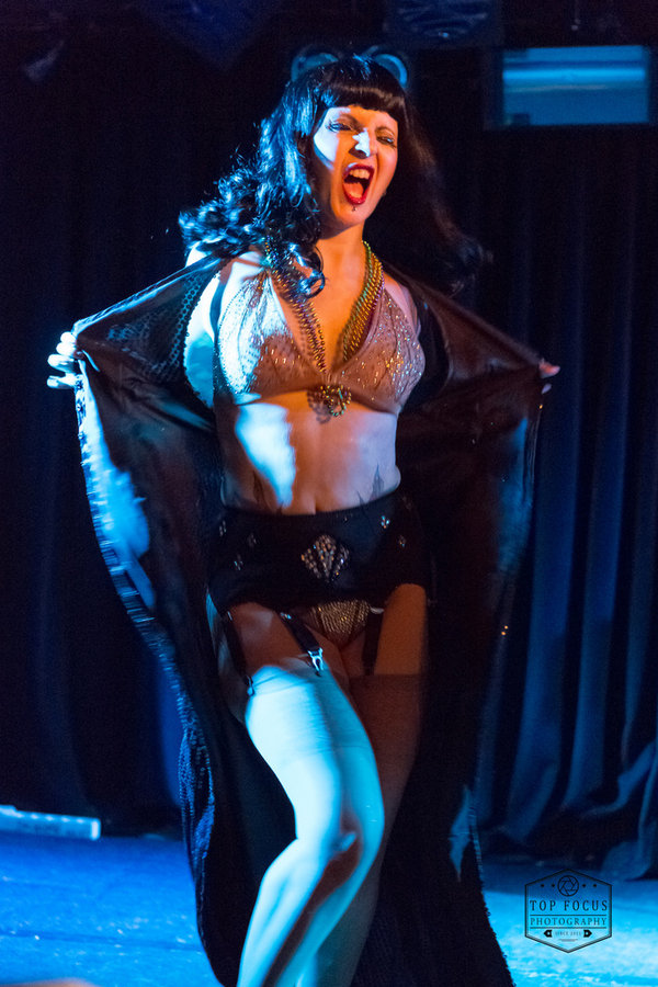 Anaïs Lune opening a dark robe to reveal a sparkly silver outfit under blue light
